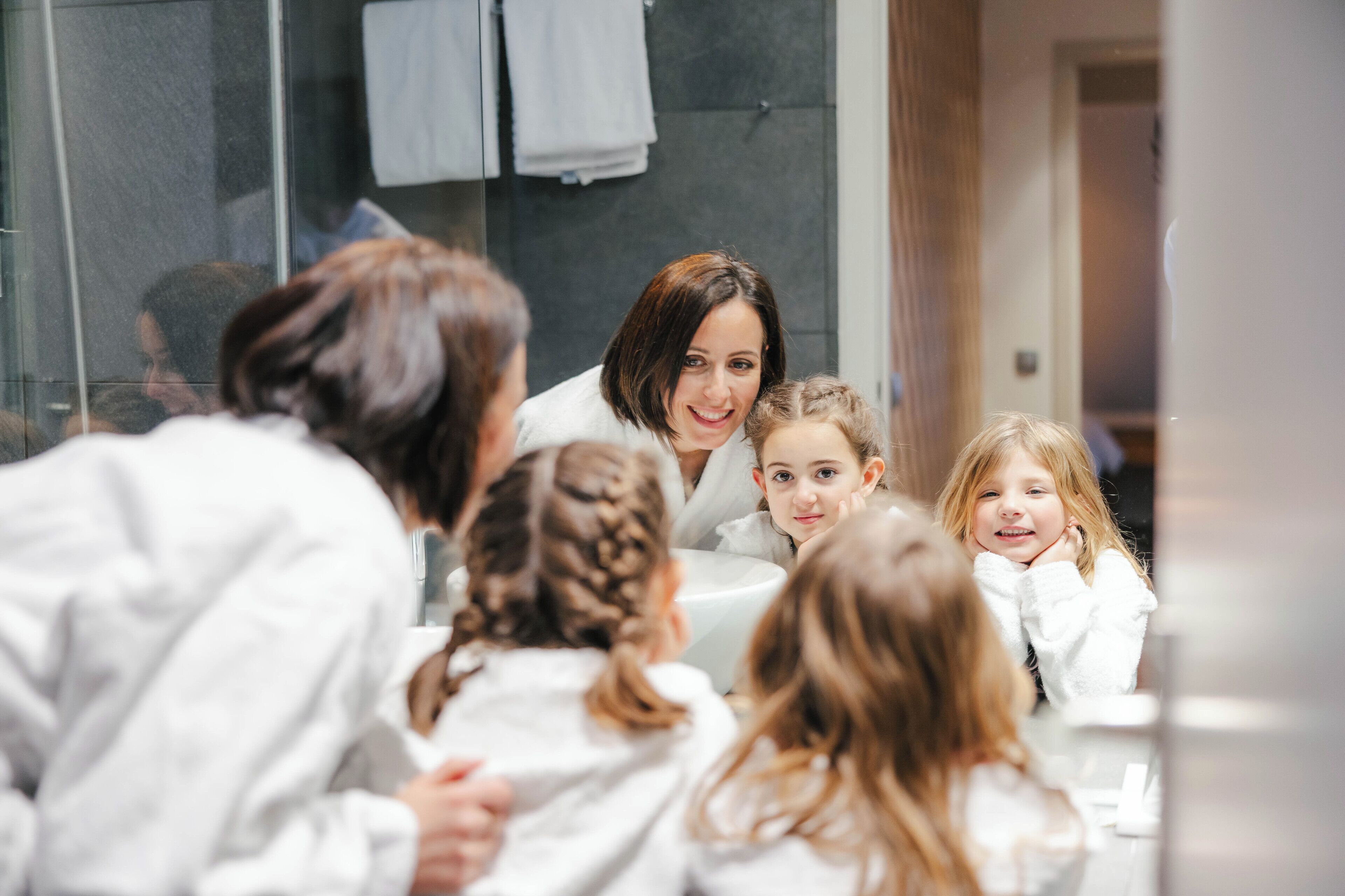 A group of people in a modern bathroom with a glass partition, a sink, and a towel rack.