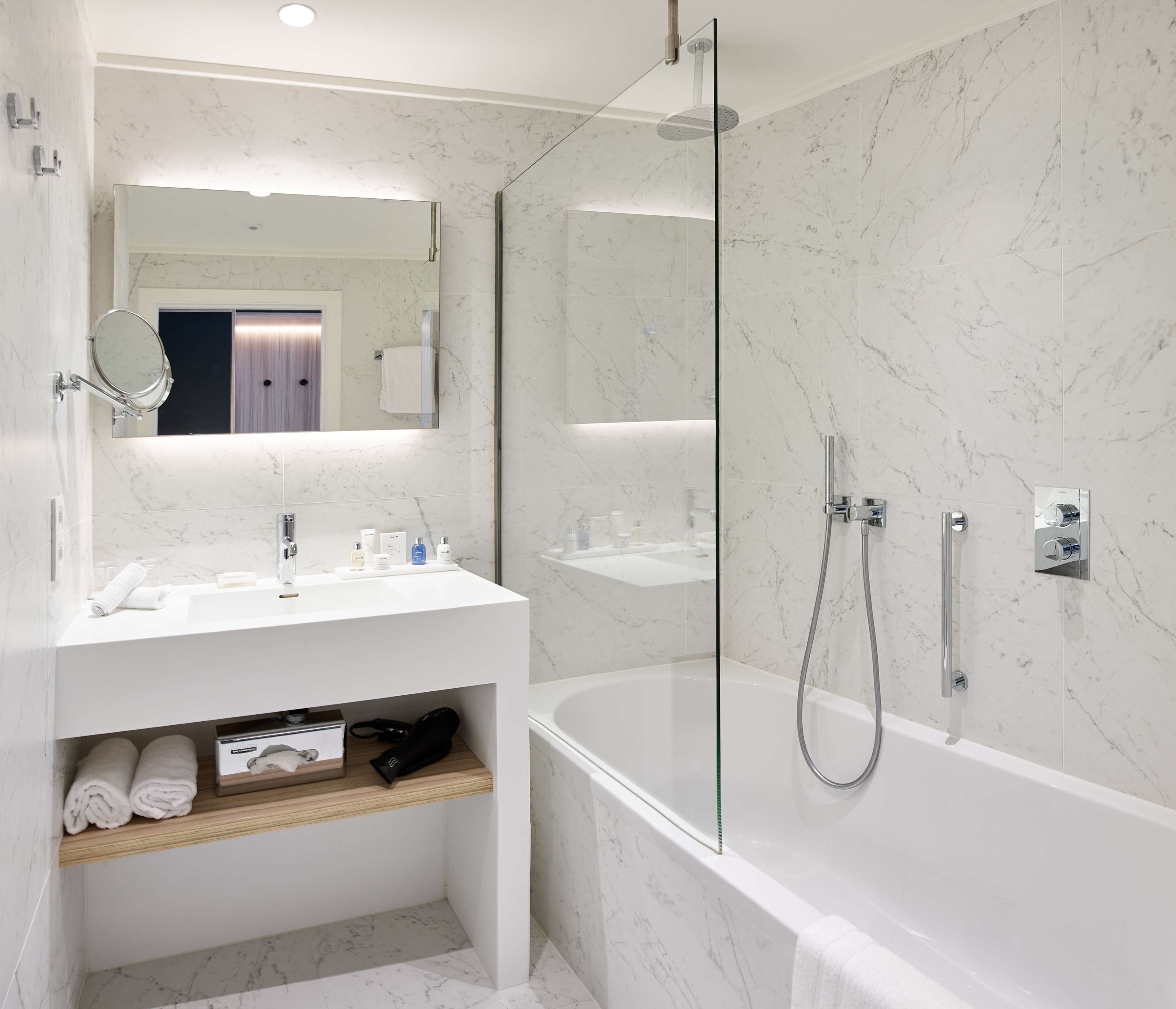 A modern bathroom with a glass-enclosed shower, a white vanity with a mirror, and a built-in shelf with towels.