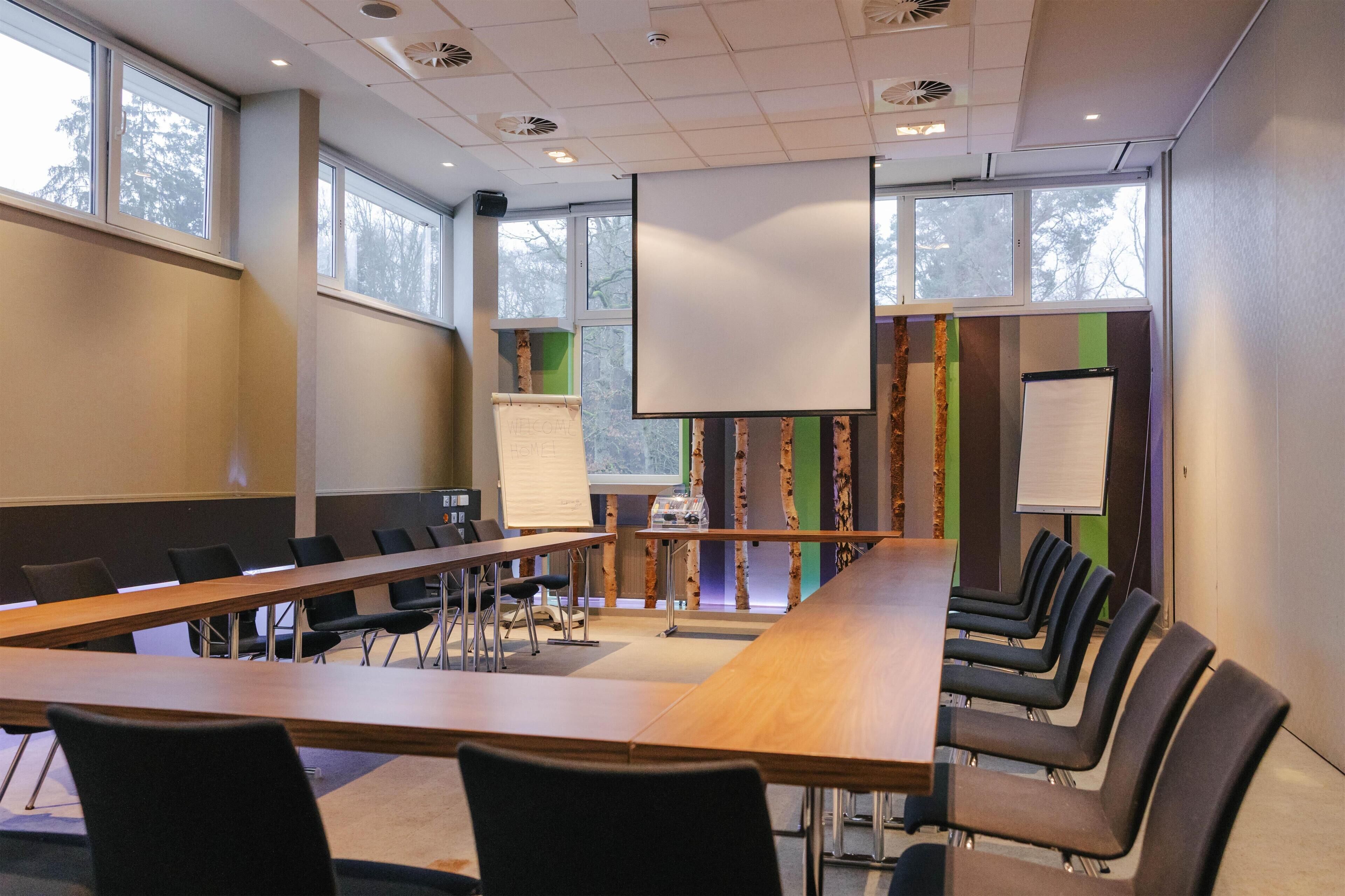 Een vergaderzaal met een lange tafel, stoelen, een whiteboard en een projectiescherm.