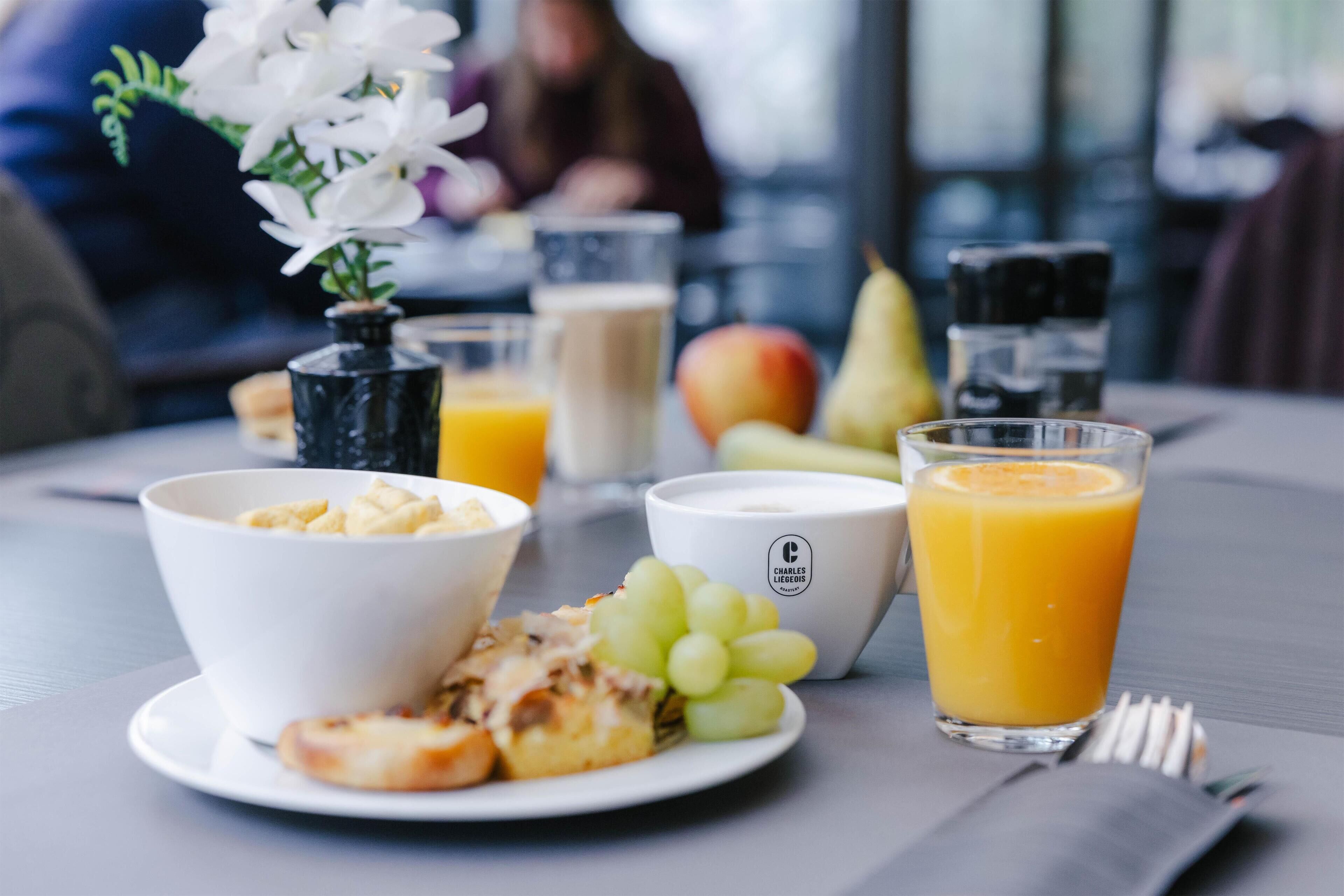 A breakfast setting with a bowl of cereal, a plate with fruit and cheese, a glass of orange juice, and a vase with flowers.