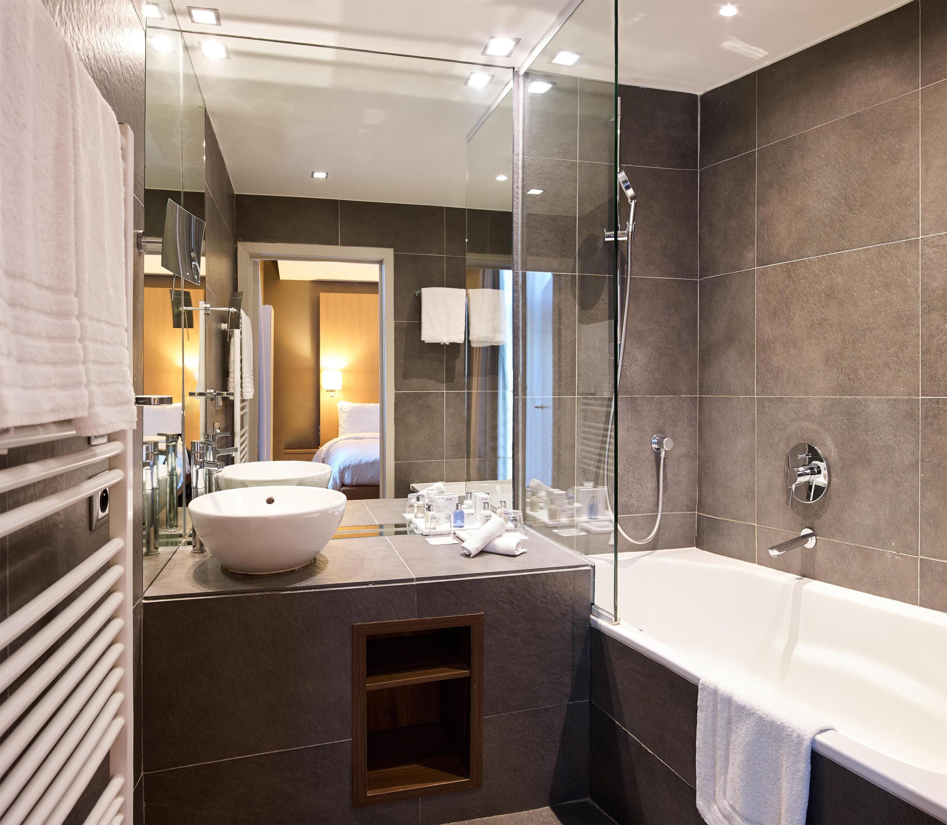 A modern bathroom with a large mirror, a bathtub, and a sink.