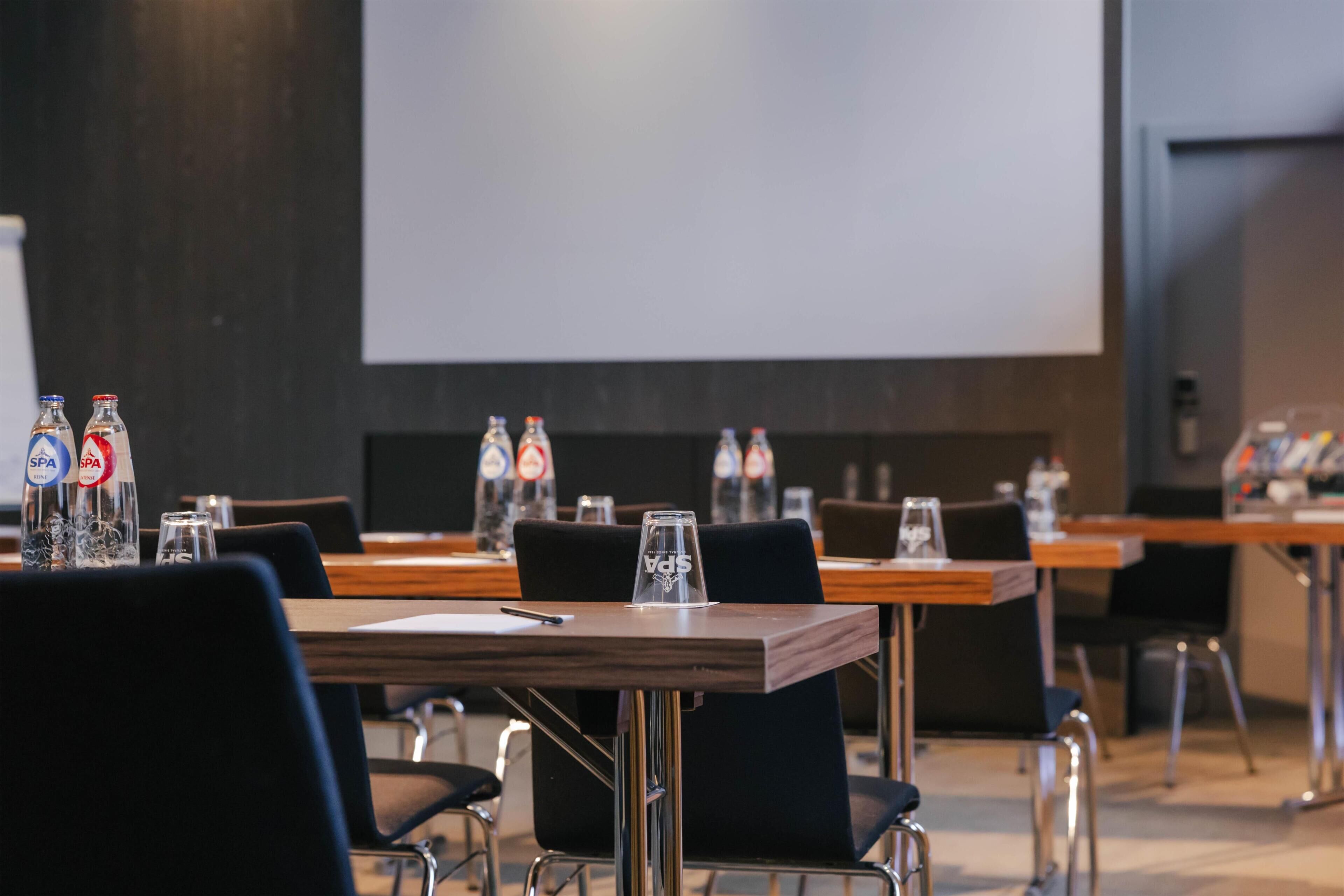 Un salón de conferencias con mesas, sillas y botellas de agua.