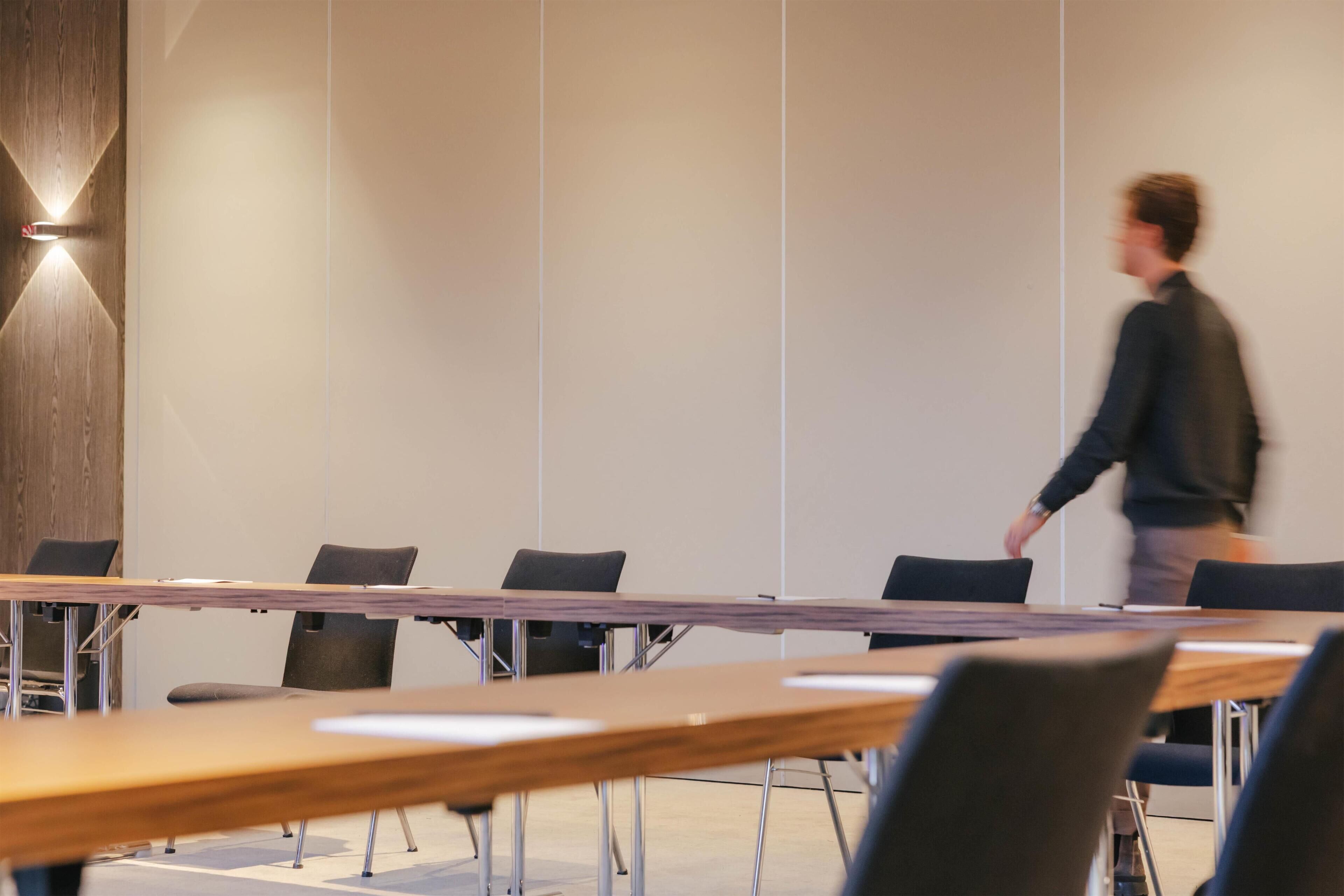 A conference room with a long table, black chairs, and a wooden accent wall.