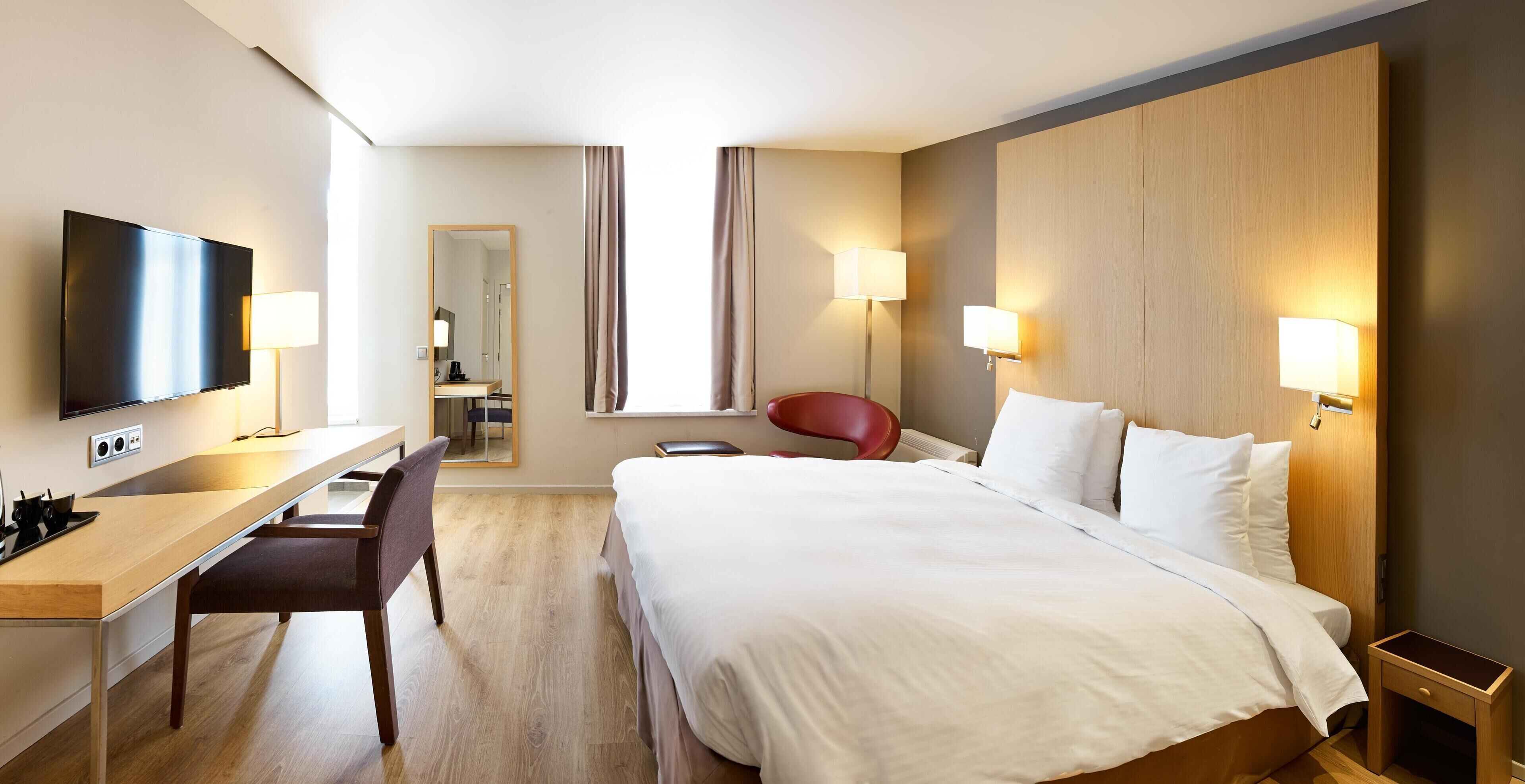 Habitación de hotel con cama, escritorio, silla, televisor y dos lámparas de noche.