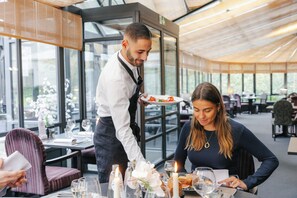 Un restaurante con un interior moderno, ventanas amplias y un camarero sirviendo comida a un cliente.
