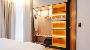 Un dormitorio con cama, un armario de madera con estantes iluminados, perchero y mesita de noche.