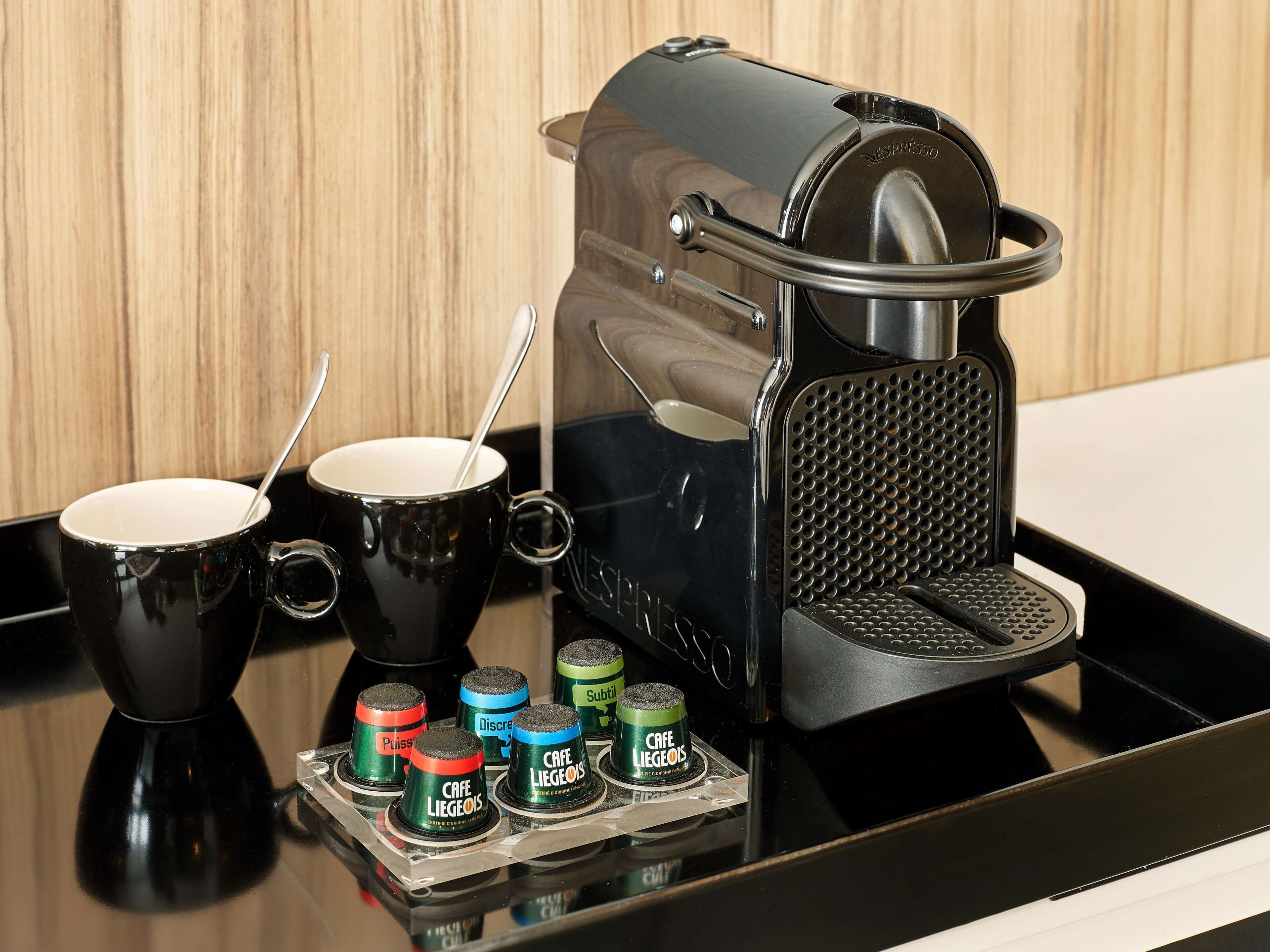 A Nespresso coffee machine with two black cups and a tray of coffee capsules.