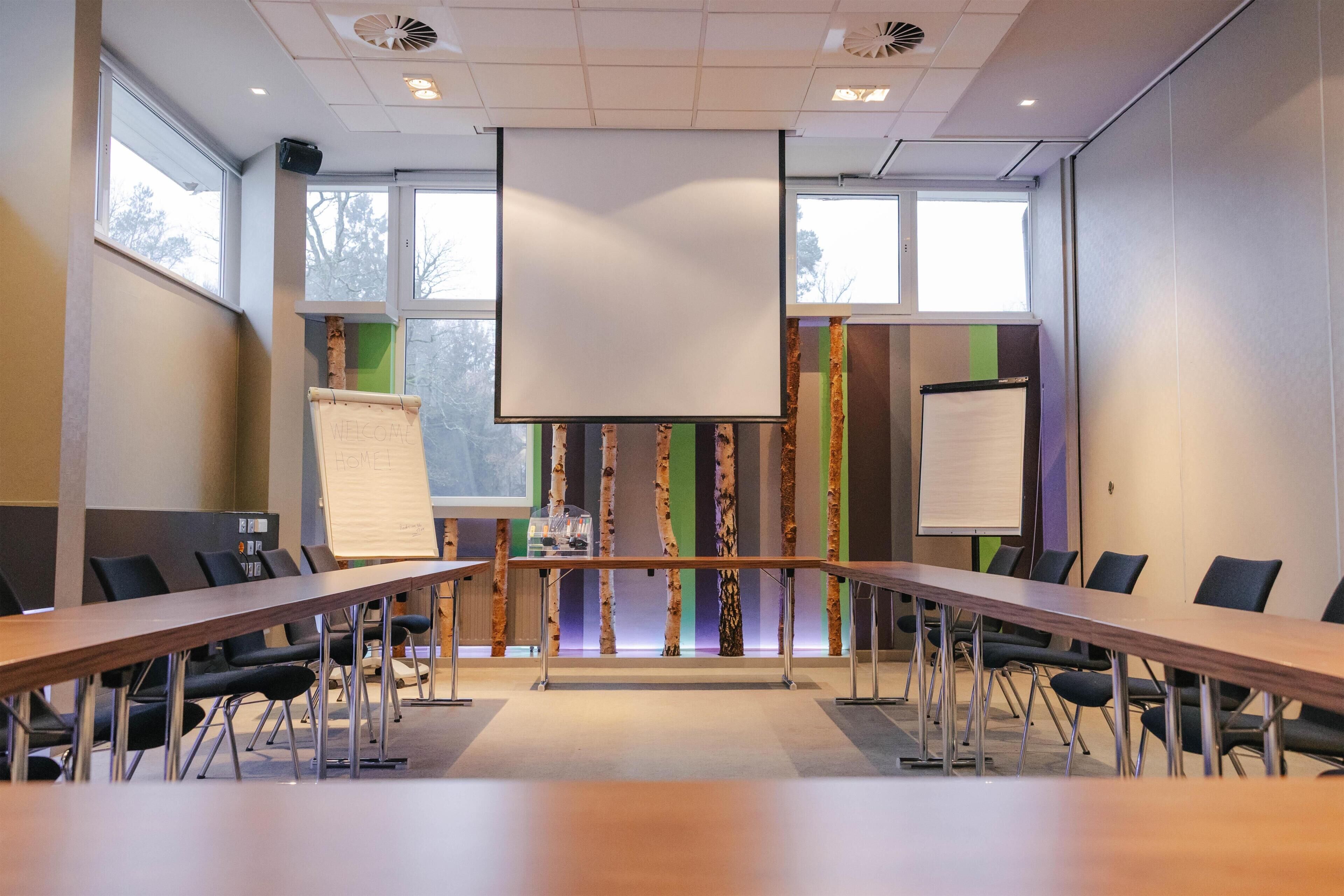 A conference room with a long table, chairs, a whiteboard, and a projector screen.