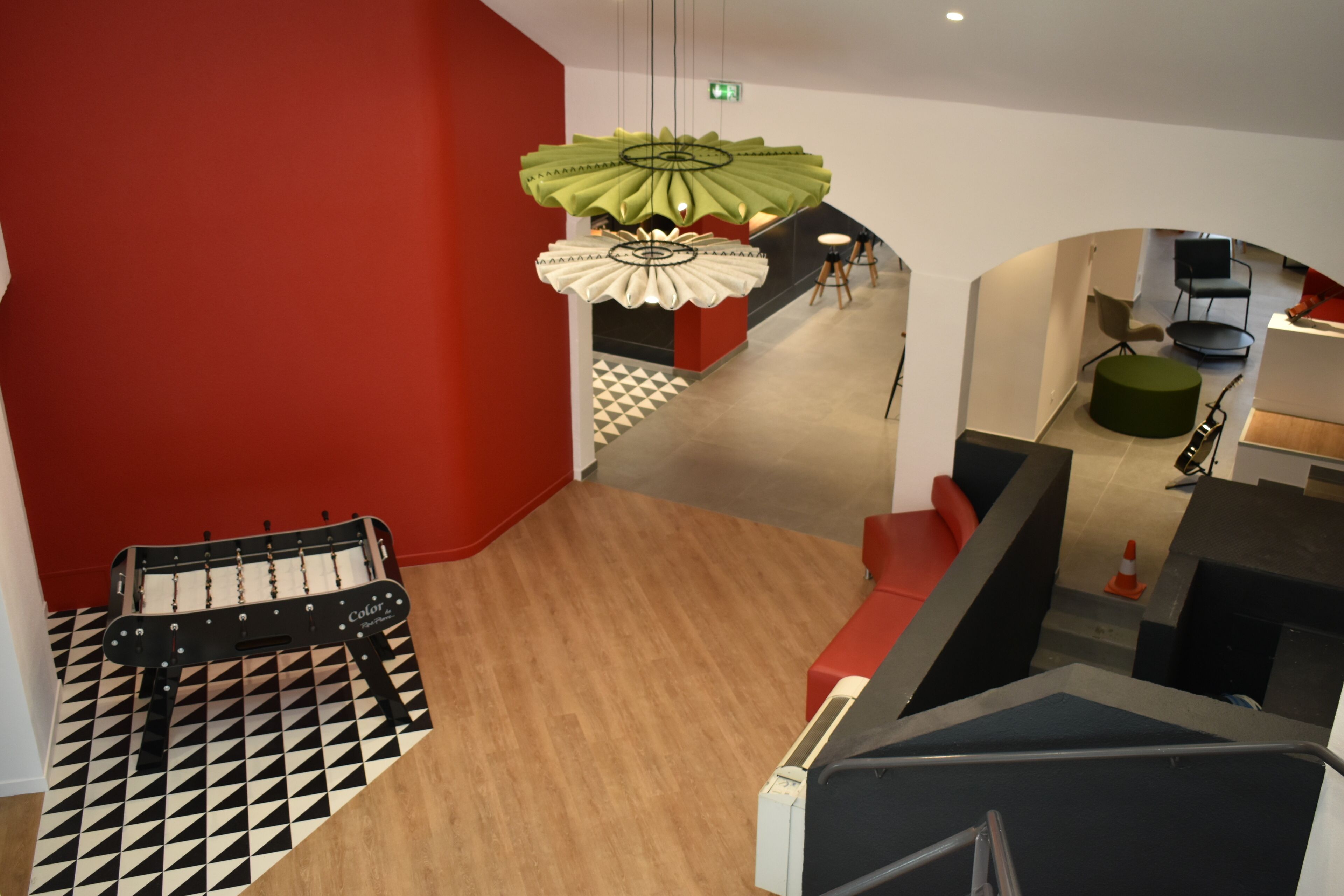 A modern interior with a checkered floor, a green hanging light fixture, and a red accent wall.