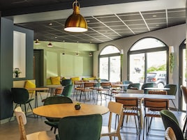 Un café moderno con varias zonas de estar, incluyendo mesas y sillas, bajo un techo con diseño de cuadrícula y lámparas colgantes.