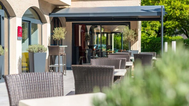 An outdoor patio with wicker furniture, a covered seating area, and potted plants.