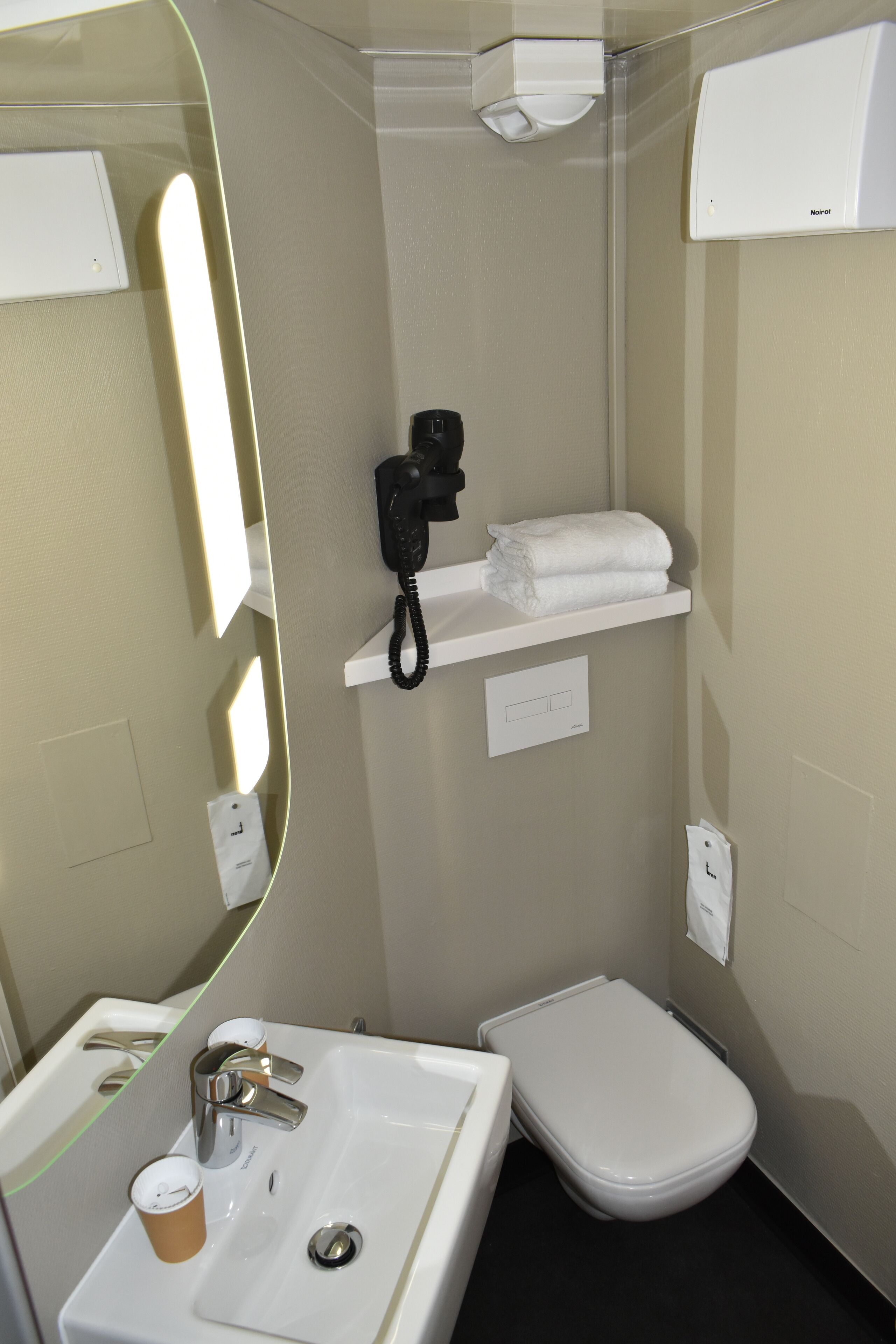 A small, modern bathroom with a white sink, a toilet, a mirror, and a towel rack.