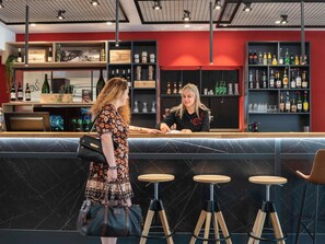A bar area with a counter, stools, and shelves stocked with bottles. - ibis Beaune Centre (Beaune)