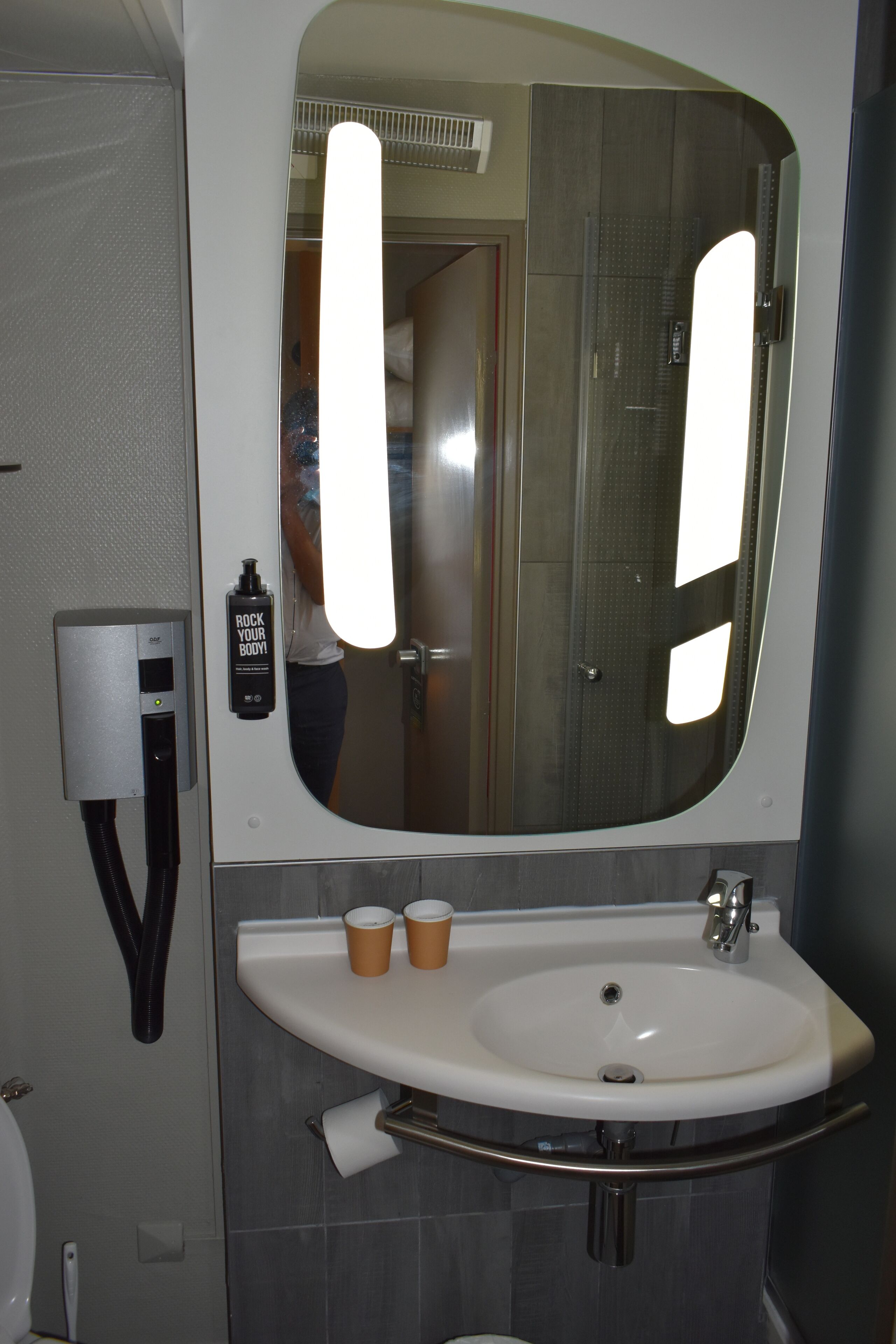 Une salle de bain avec un grand miroir, un lavabo et un sèche-mains.