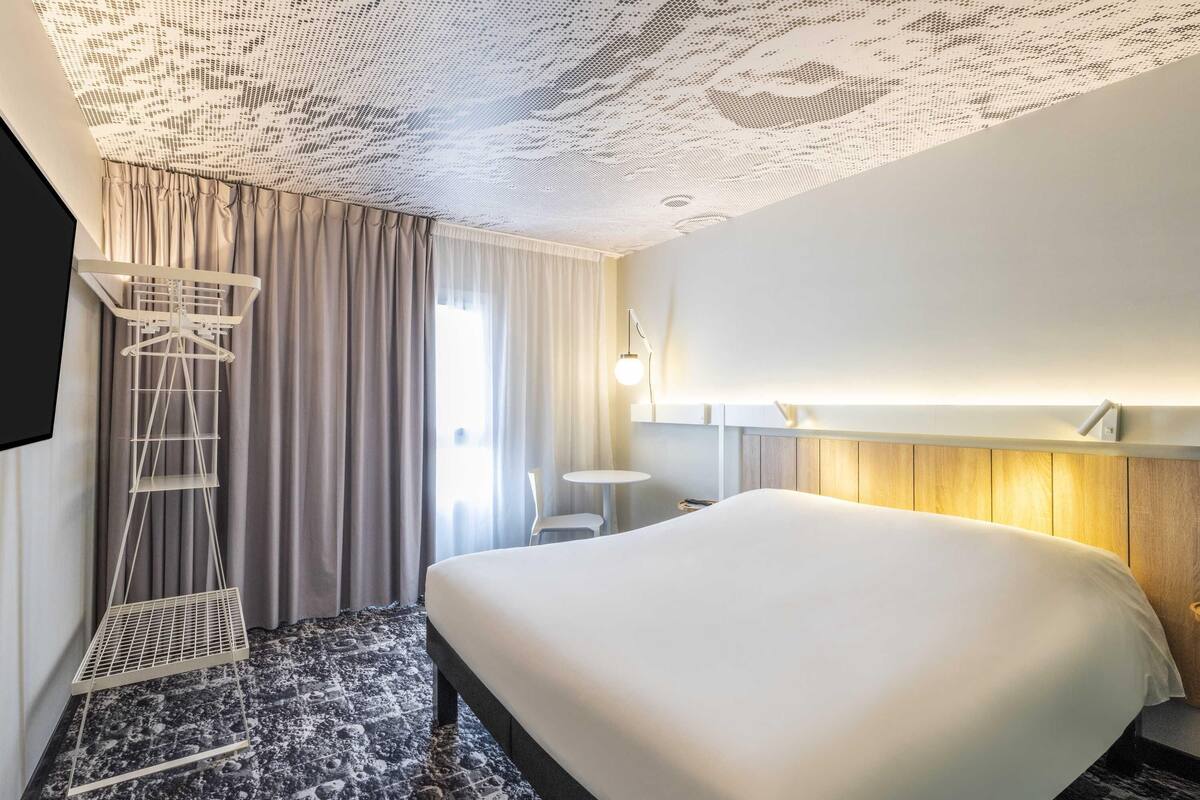Ein Hotelzimmer mit einem großen Bett, einem Schreibtisch, einem Stuhl, einem Fernseher und einer Decke mit einem einzigartigen Muster.