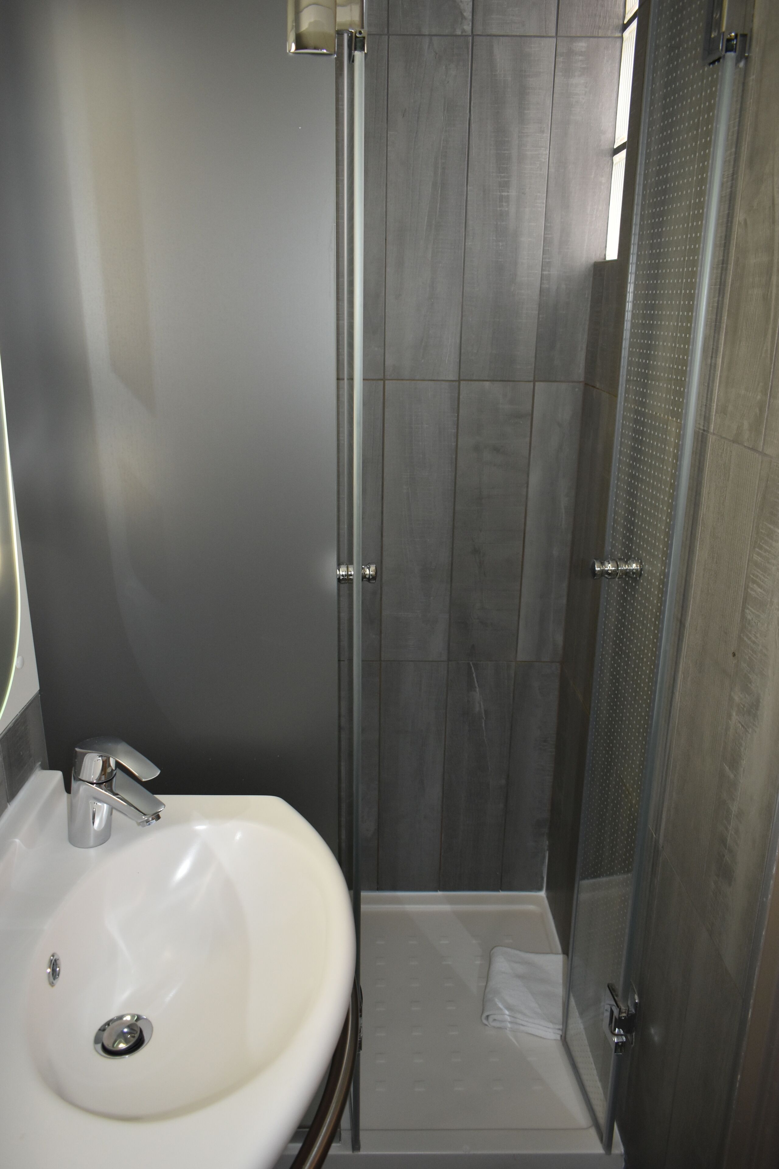 A modern bathroom with a white sink, a shower enclosure, and a tiled floor.