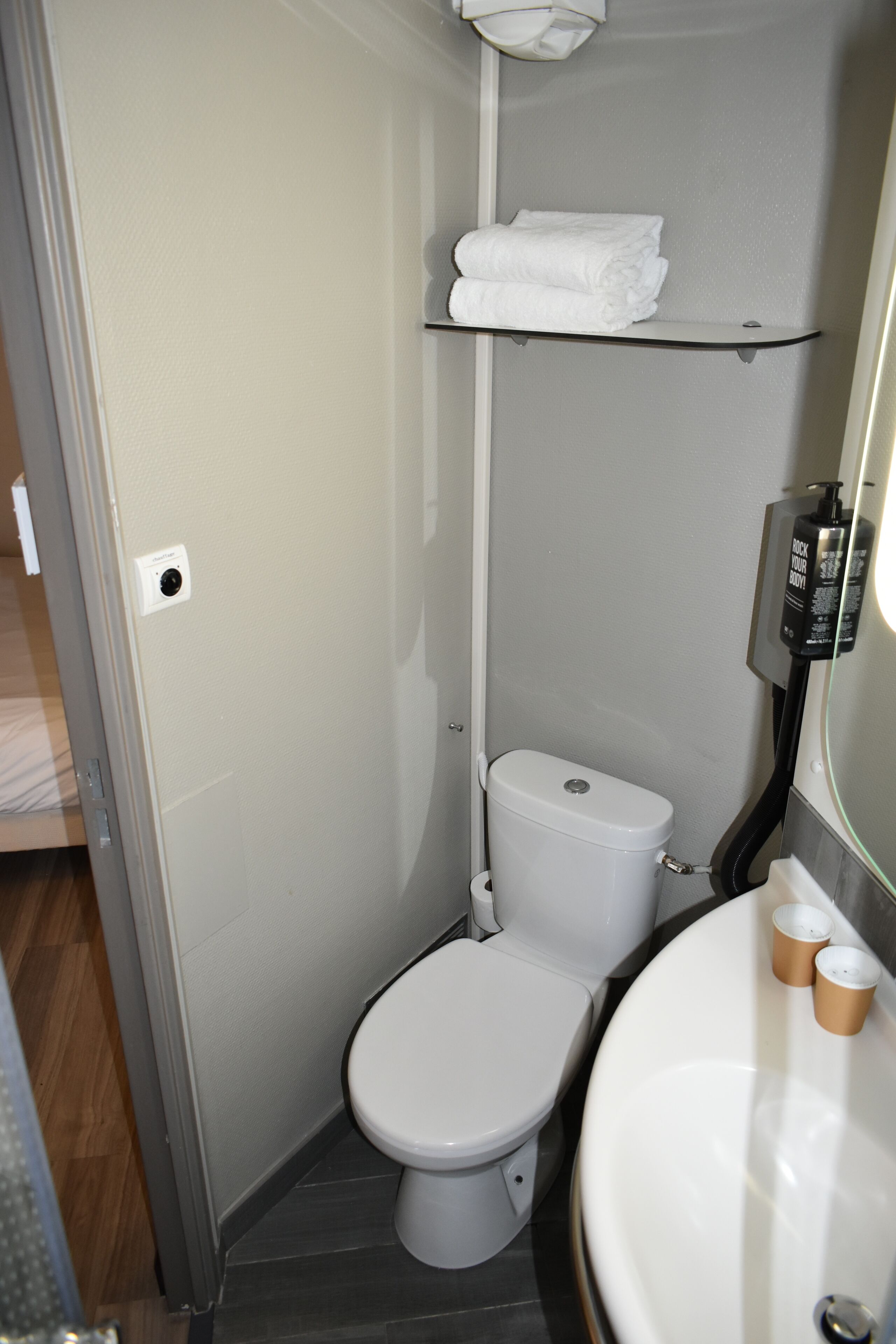 A compact bathroom with a toilet, a sink, and a shelf with towels.