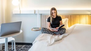 A hotel room with a bed, a bedside table, a laptop, and a reading light.