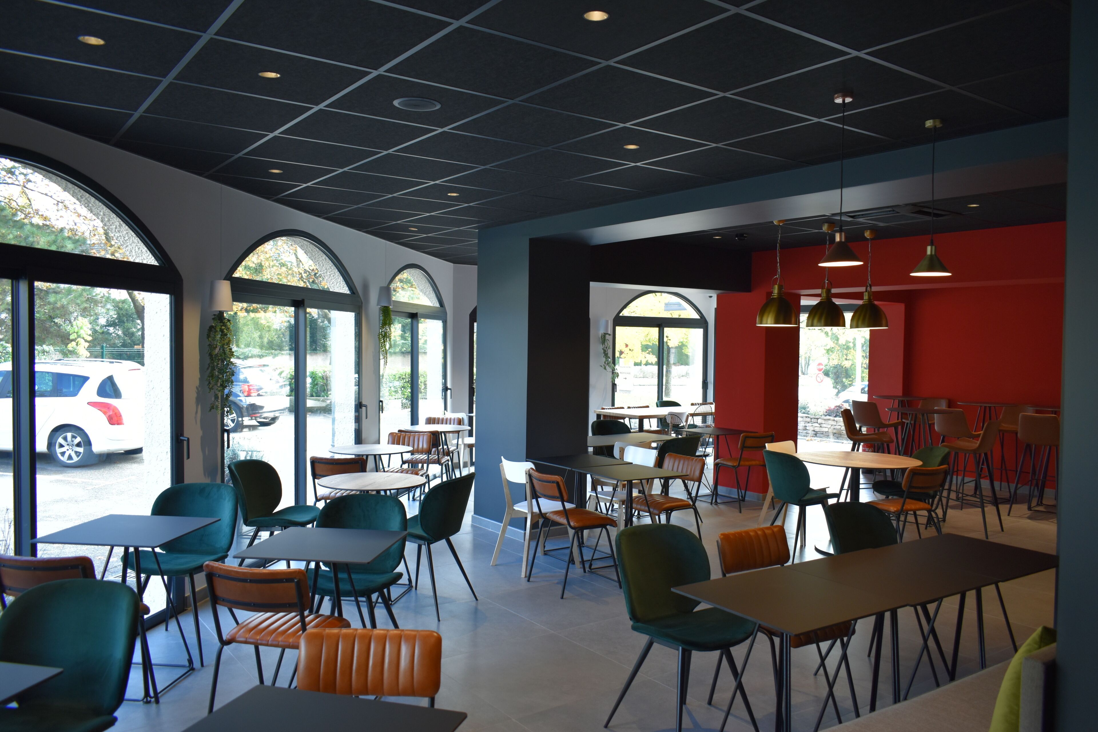 Un café moderno con mesas y sillas, ventanas amplias y una pared de acento roja.