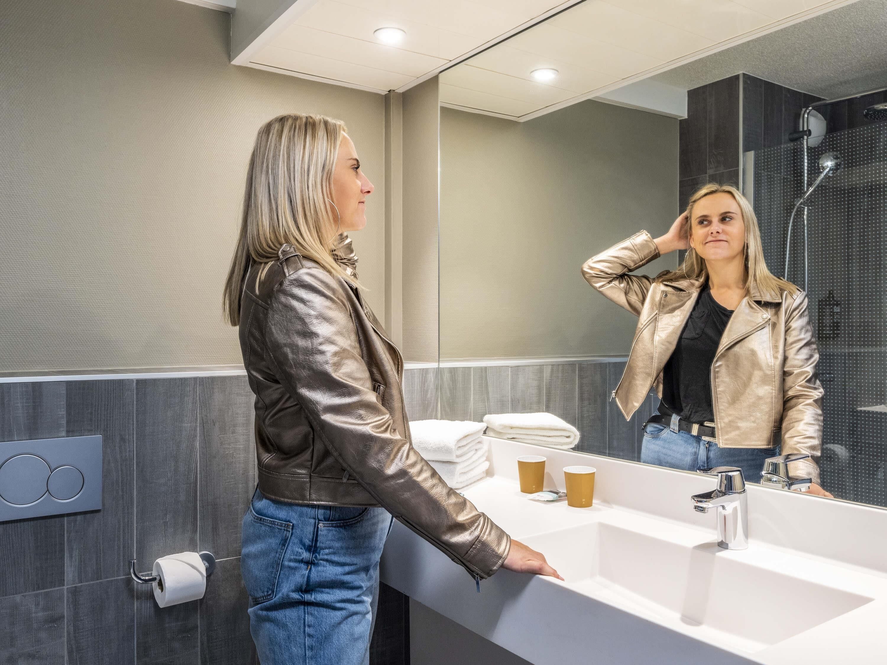 Un baño moderno con un espejo grande, un lavamanos y una ducha.