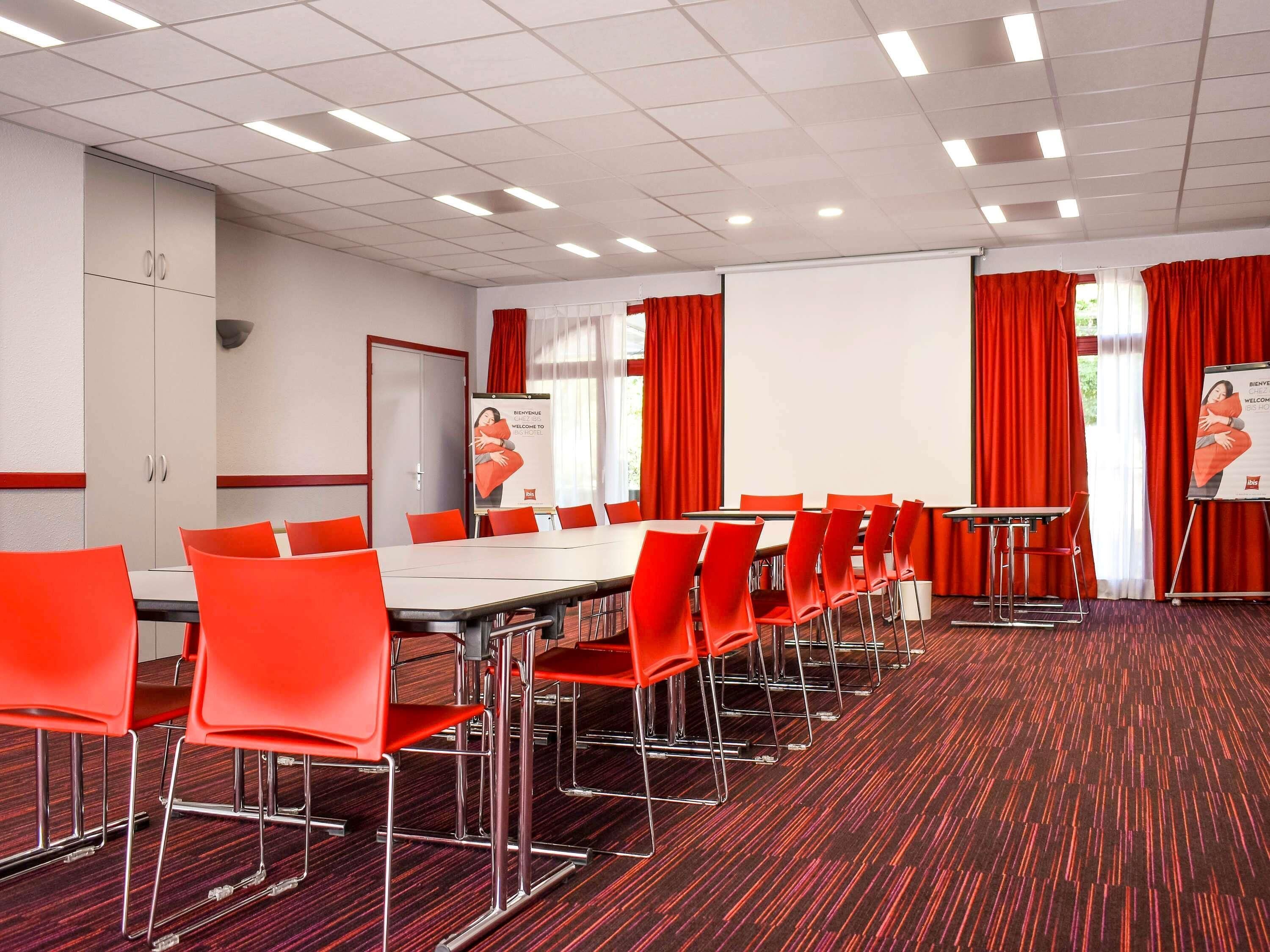 A conference room with a long table, red chairs, a whiteboard, and red curtains.
