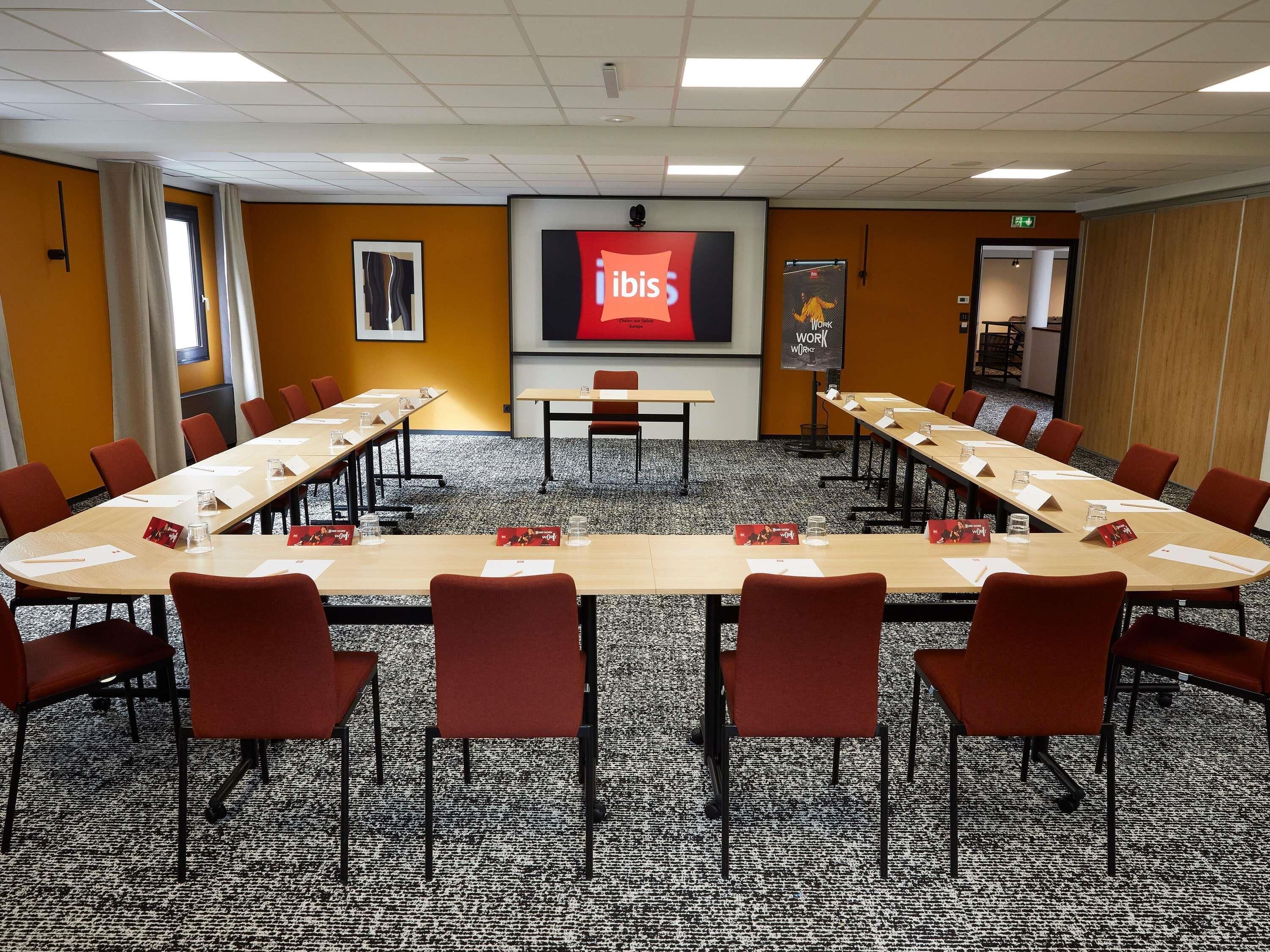 A conference room with a long table, red chairs, and a projector screen displaying 'ibis'.