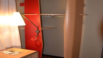 A room with a wooden floor, a red wall, a white curtain, a lamp, and a shelf.