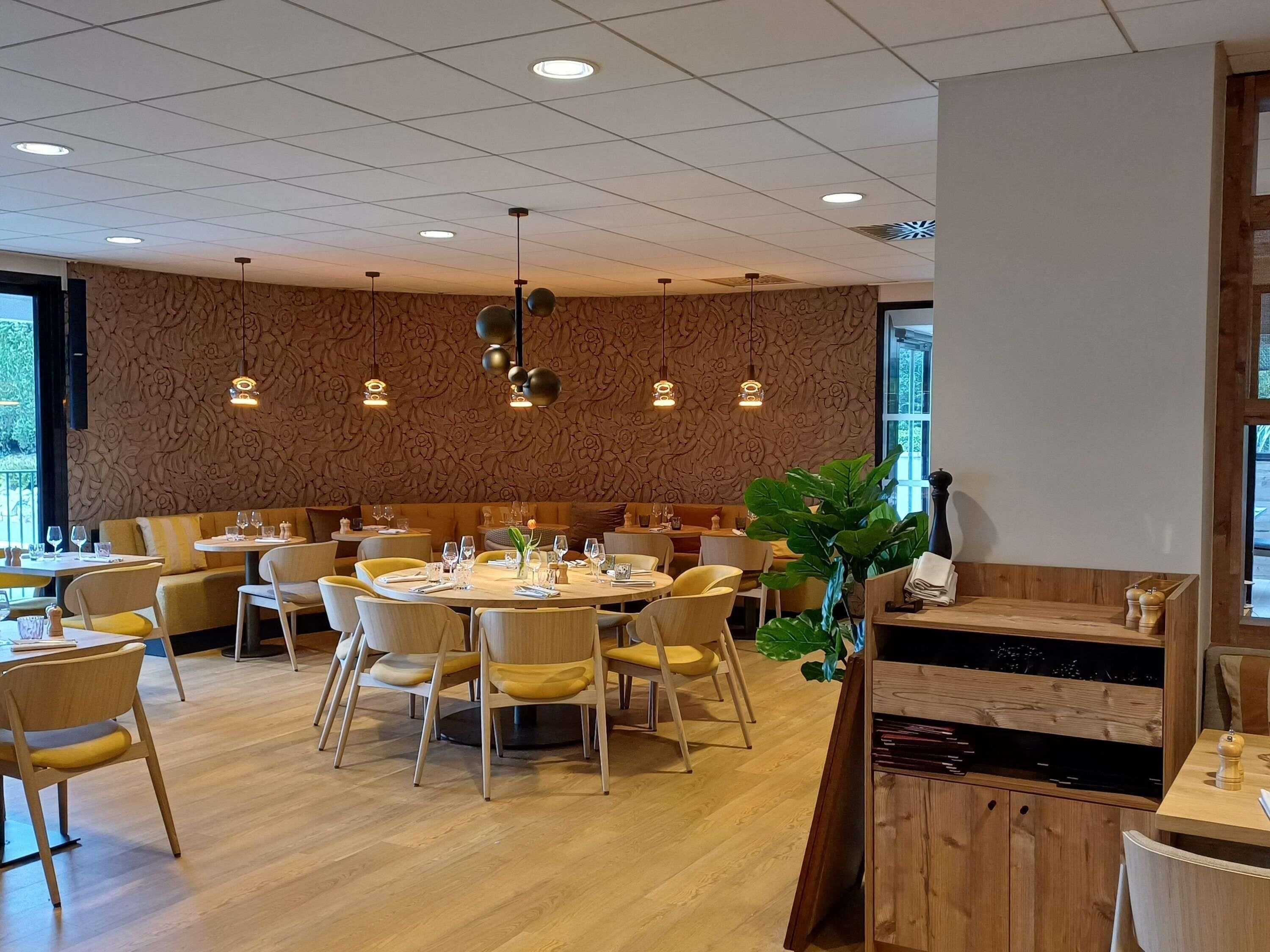 Un interno di ristorante con tavoli rotondi, sedie e una parete decorata.