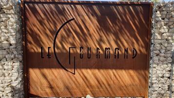 Une enseigne métallique portant l’inscription « LE GOURMAND » et un logo stylisé en forme de « G ».