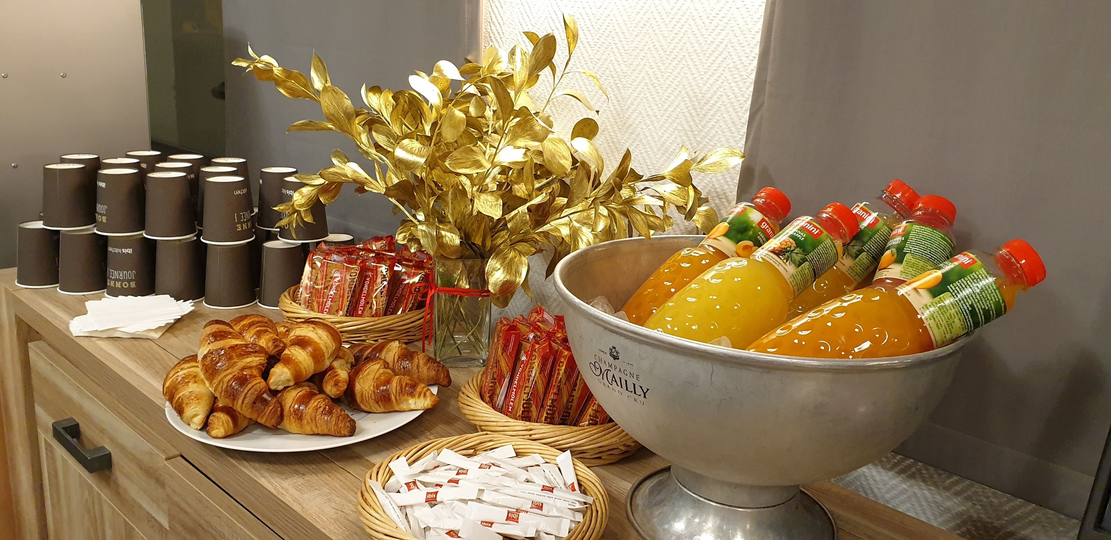 Una mesa de buffet con croissants, pasteles y un tazón de jugos de frutas.