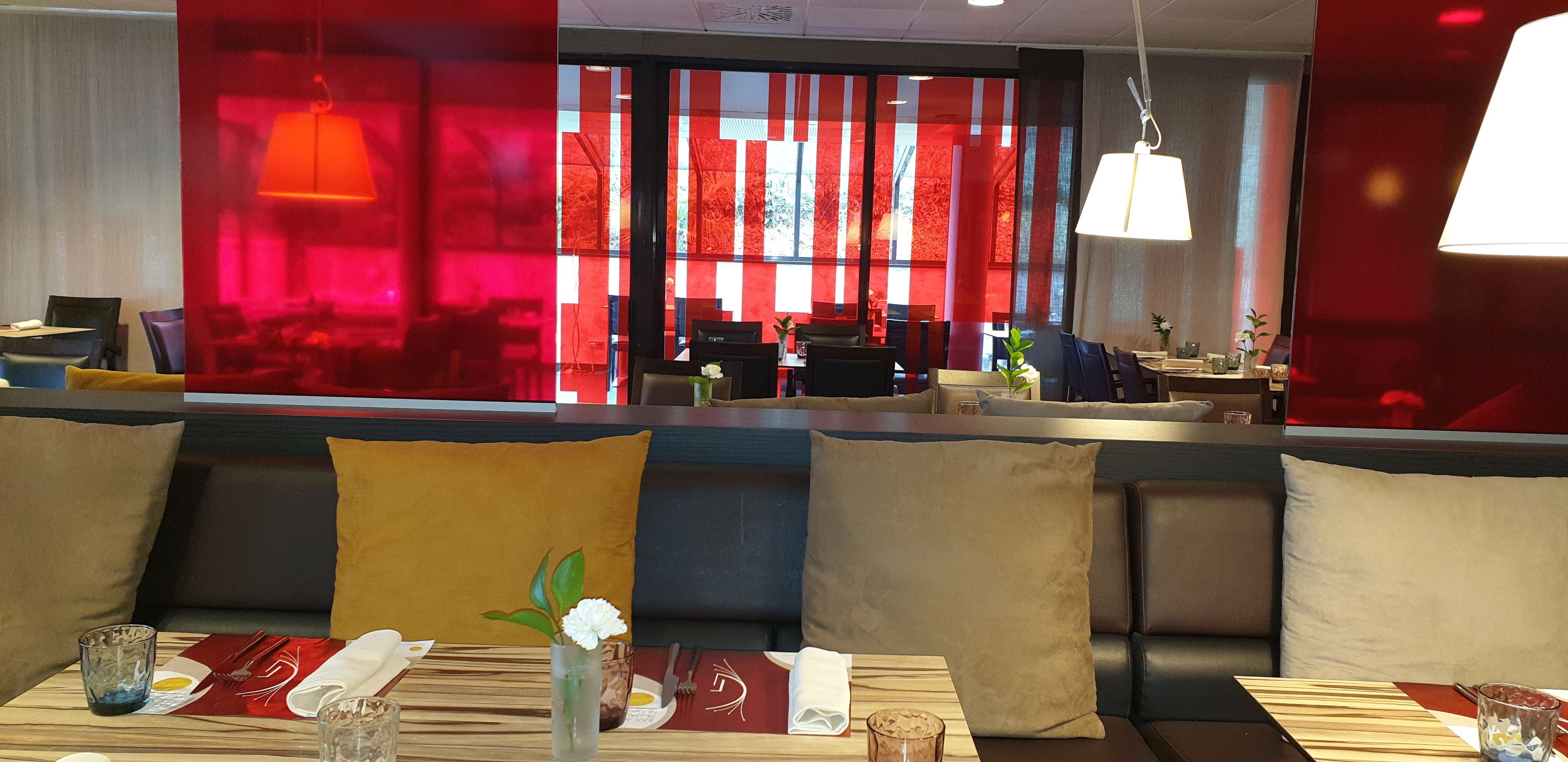 A restaurant with a modern interior, featuring a seating area with cushioned benches and a dining table set with cutlery and a vase of flowers.