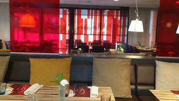 A restaurant with a modern interior, featuring a seating area with cushioned benches and a dining table set with cutlery and a vase of flowers.