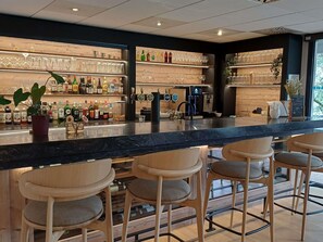Zona de bar con taburetes de madera, estantes con botellas de licores y una máquina de café.