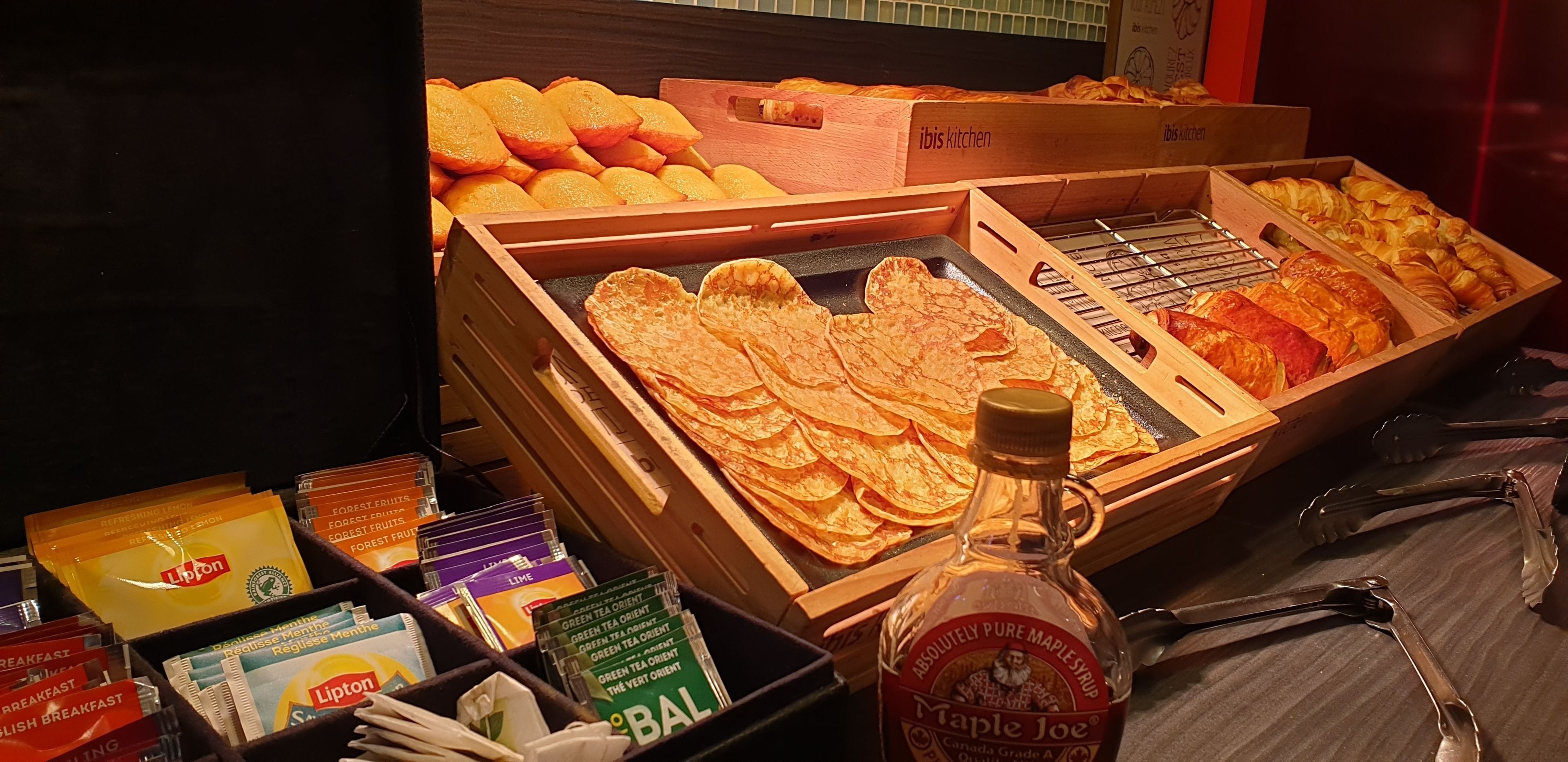 A breakfast display with various pastries, a bottle of maple syrup, and Lipton tea packets.