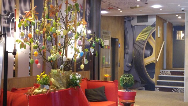 Een moderne lobby met een rode bank, een decoratieve boom met kleurrijke versieringen, en een spiltrap op de achtergrond.