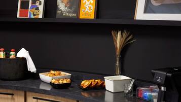 A kitchen counter with a coffee machine, a bowl of croissants, a vase with dried plants, and a book titled 'Velázquez'.