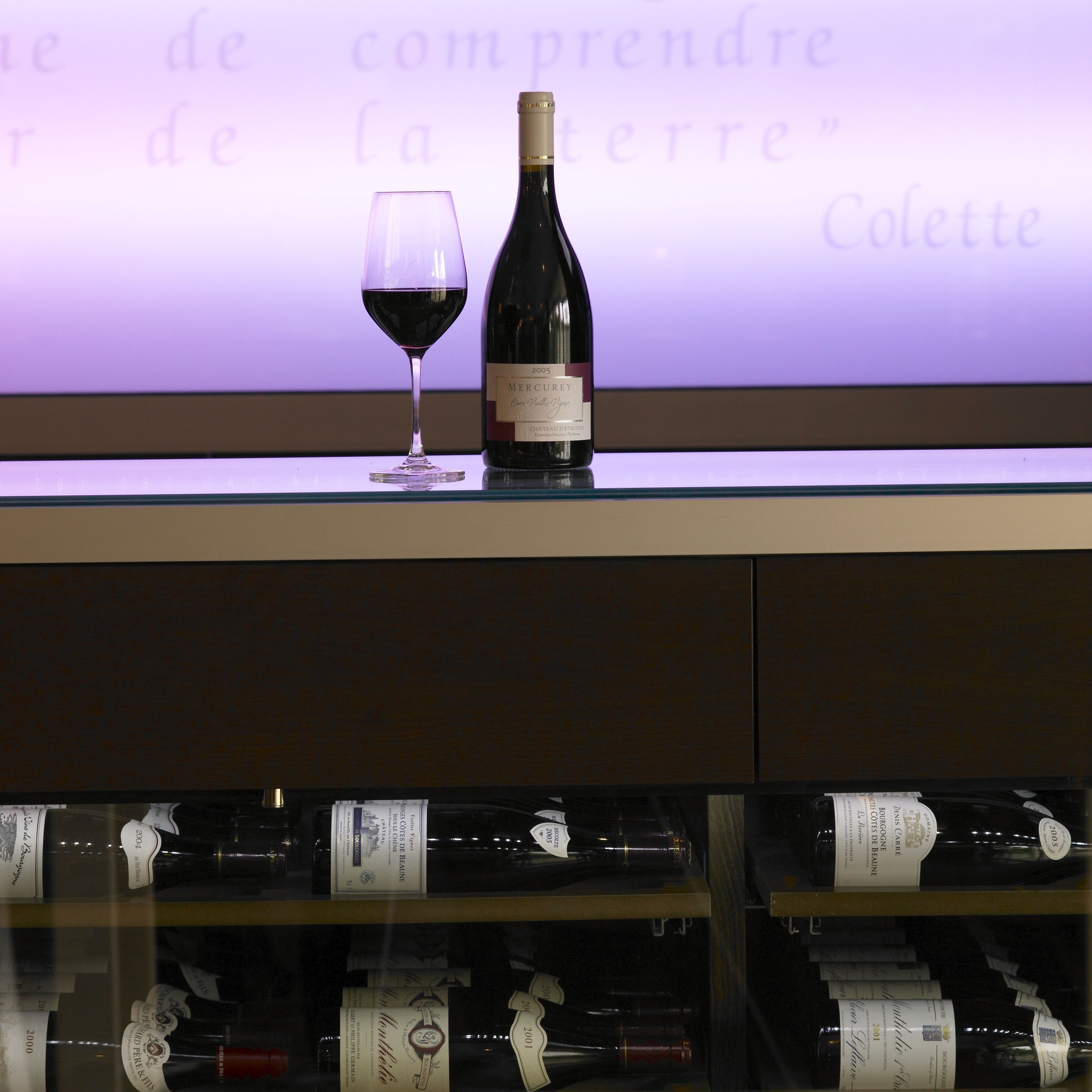 Una botella de vino y una copa sobre una encimera, con fondo morado y texto.