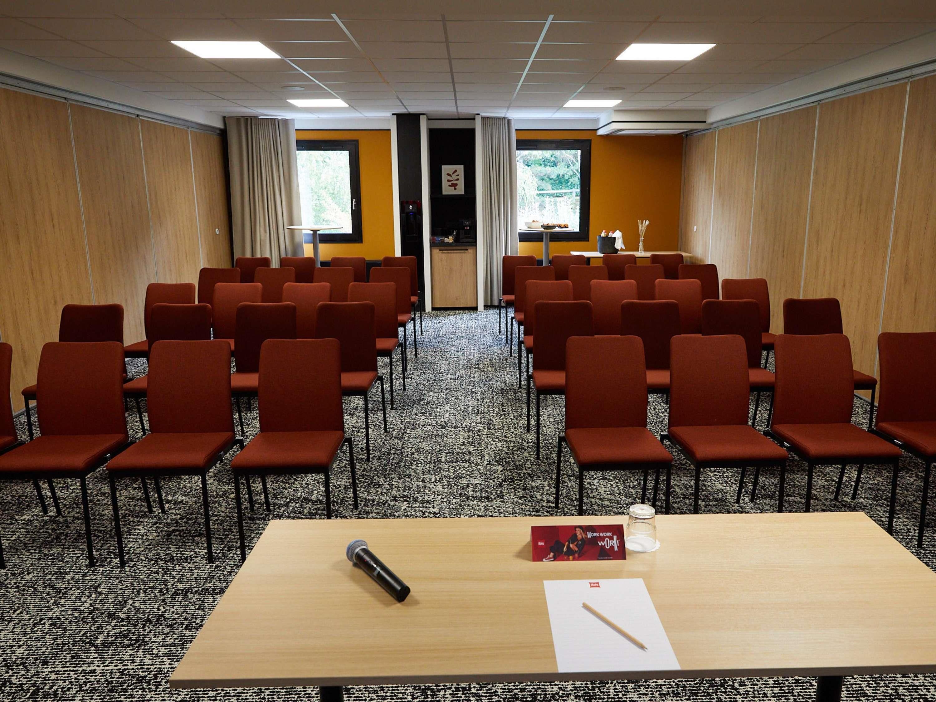 A conference room with rows of chairs, a podium, a table with a microphone, a candle, and a book.