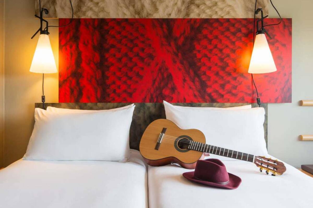 Una habitación de hotel con una cama, una guitarra y un sombrero sobre la cama.