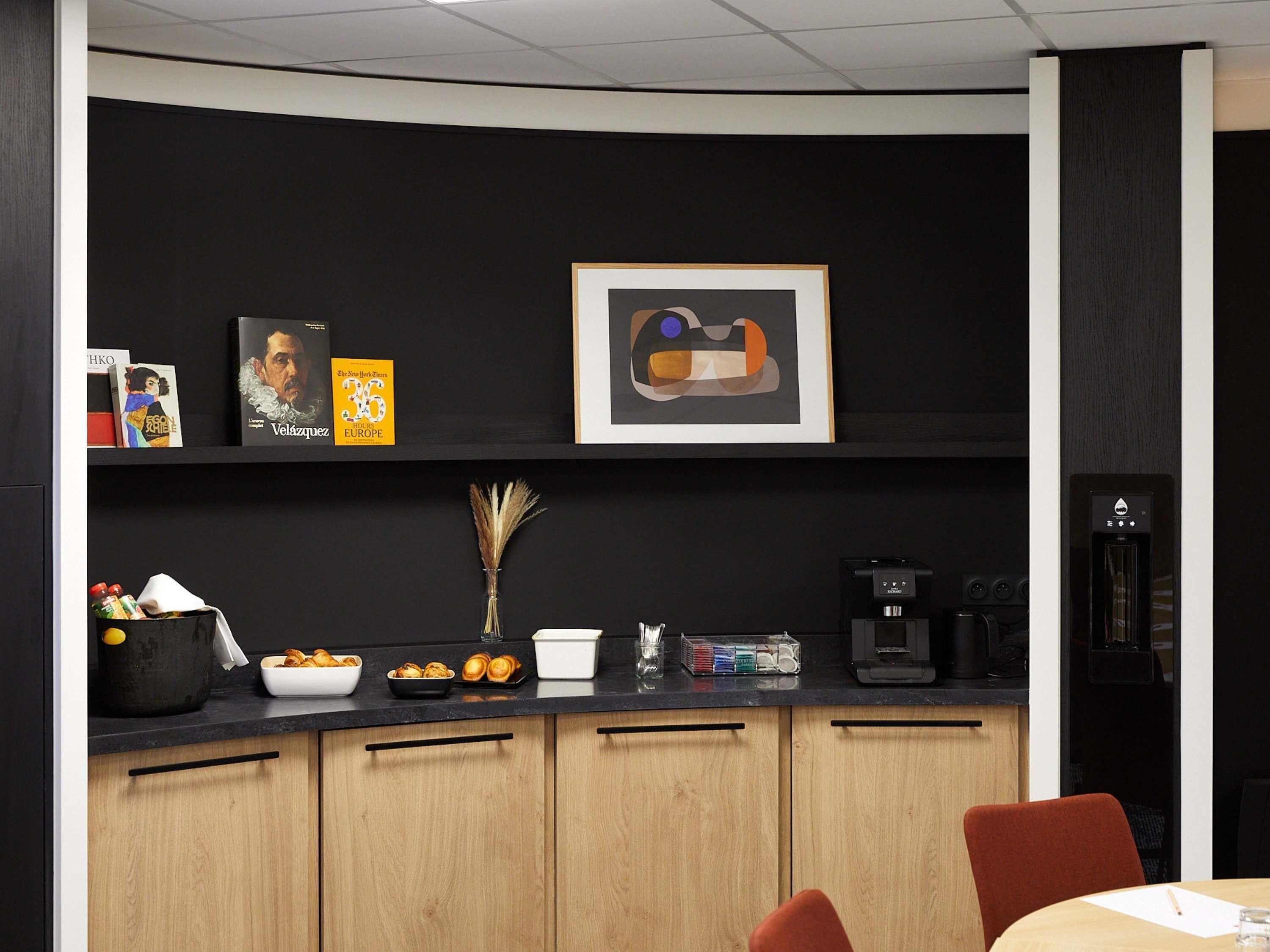 A modern kitchen with a black countertop, wooden cabinets, a coffee machine, and a framed abstract painting.