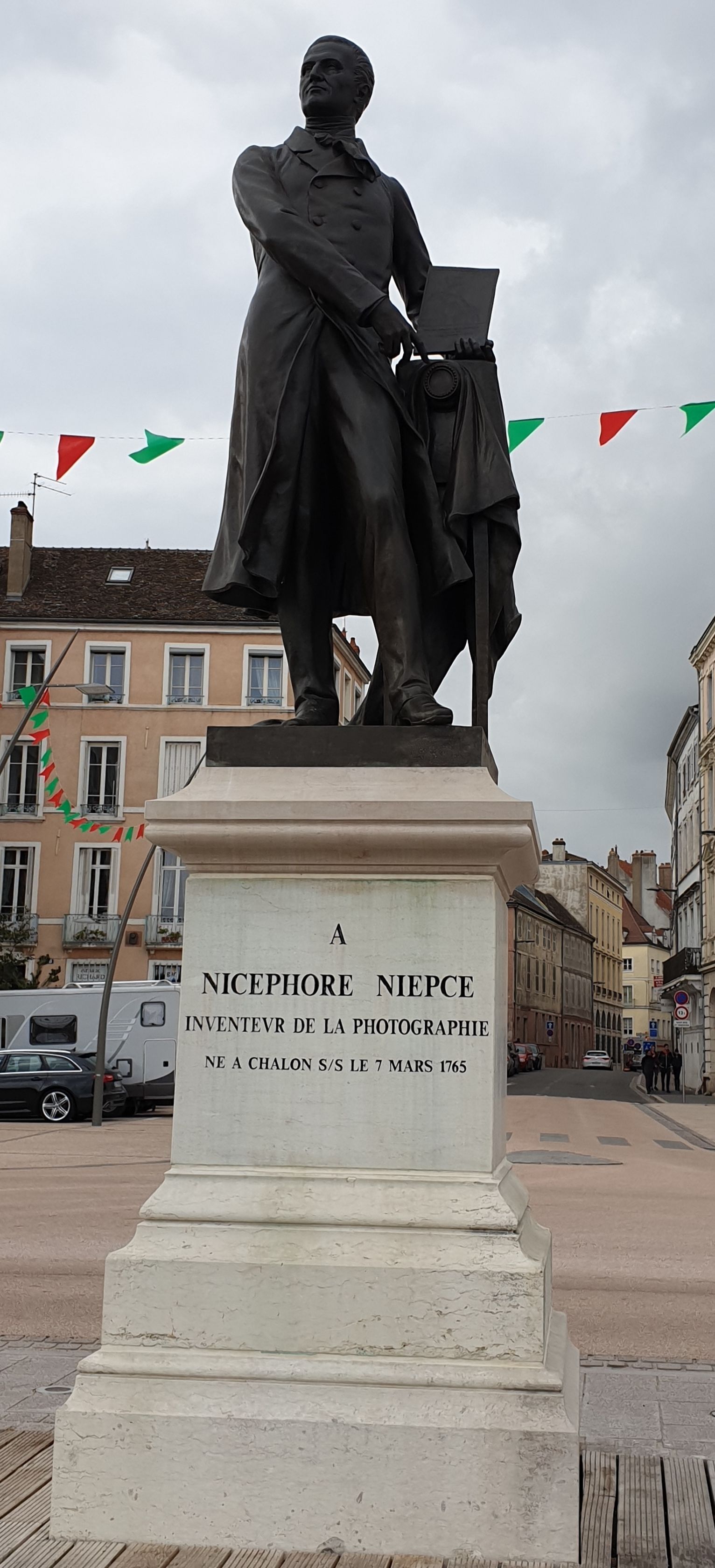 A statue of Nicephore Niepce holding a camera, with a plaque that reads "Inventeur de la Photographie" and "Ne a Chalon S/L 7 Mars 1765".