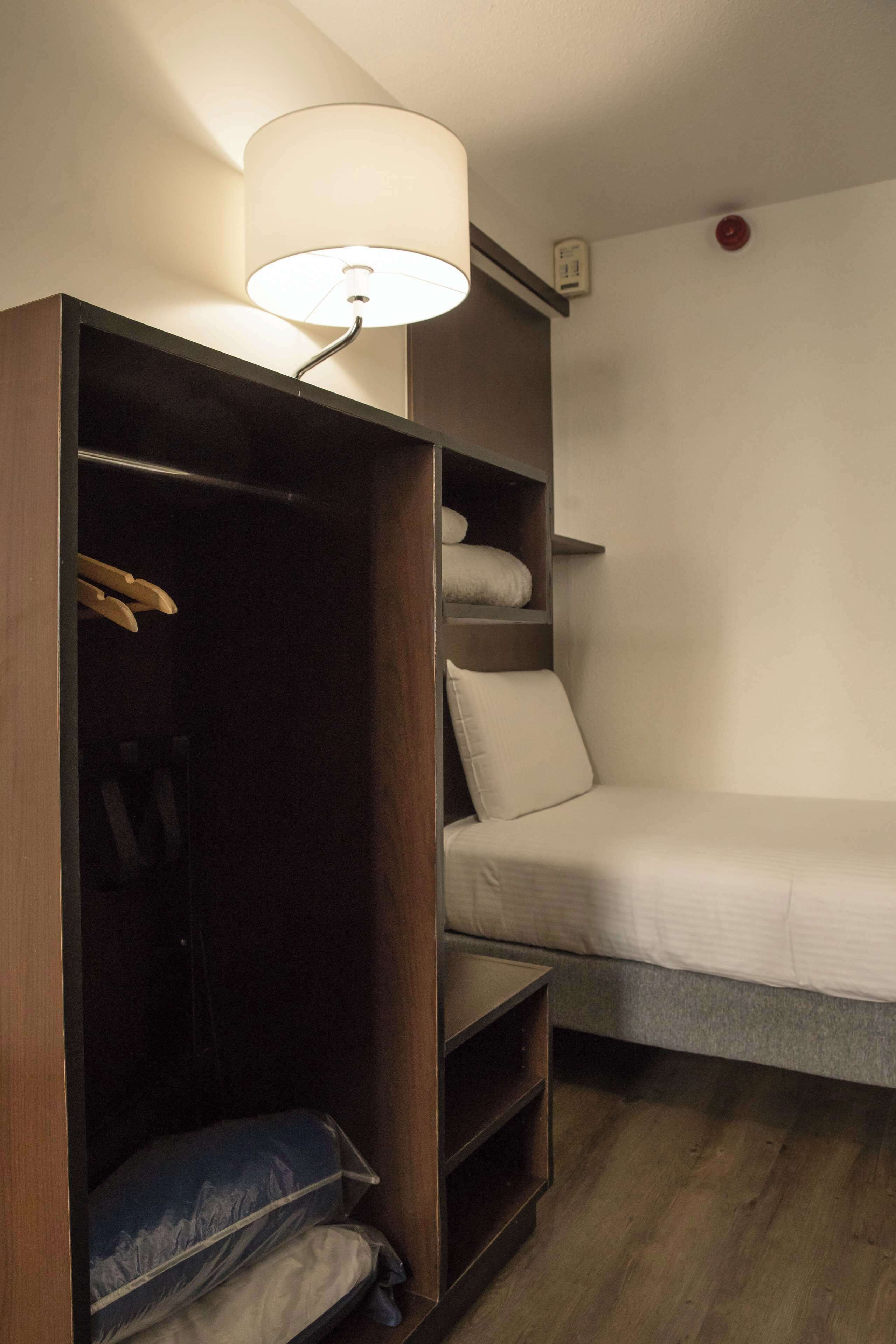 A compact room with a bed, a wardrobe, and a bedside table.
