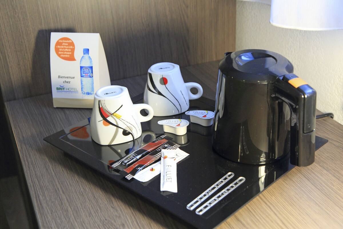 A hotel room's breakfast tray with a coffee maker, two cups, a water bottle, and a Brit Hotel brochure.