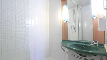 Ein Badezimmer mit einem grünen Waschbecken, einer Duschkabine aus Glas und weiß gefliesten Wänden.