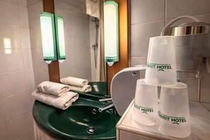 Un baño de hotel con un lavabo verde, dos vasos apilados con el logotipo de Brit Hotel y toallas sobre el mostrador.