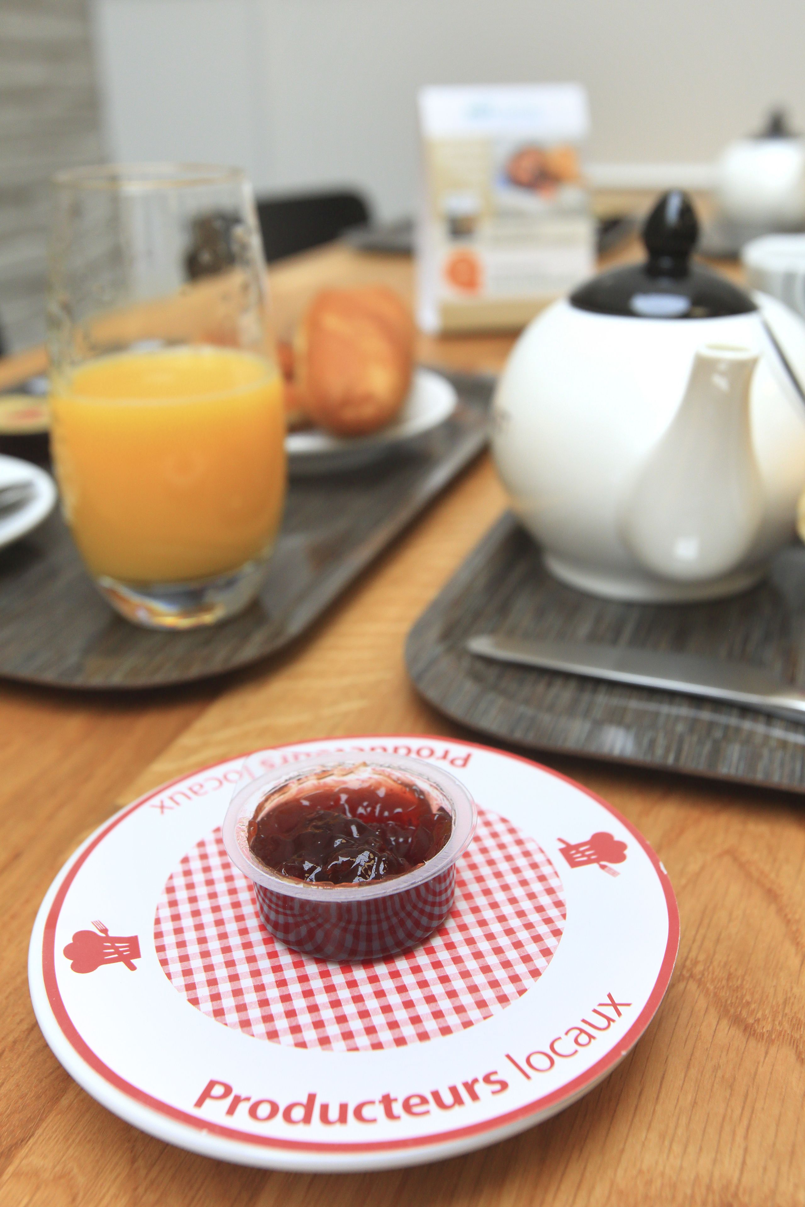 A breakfast setting with a plate of jam, a glass of orange juice, and a teapot on a wooden table.