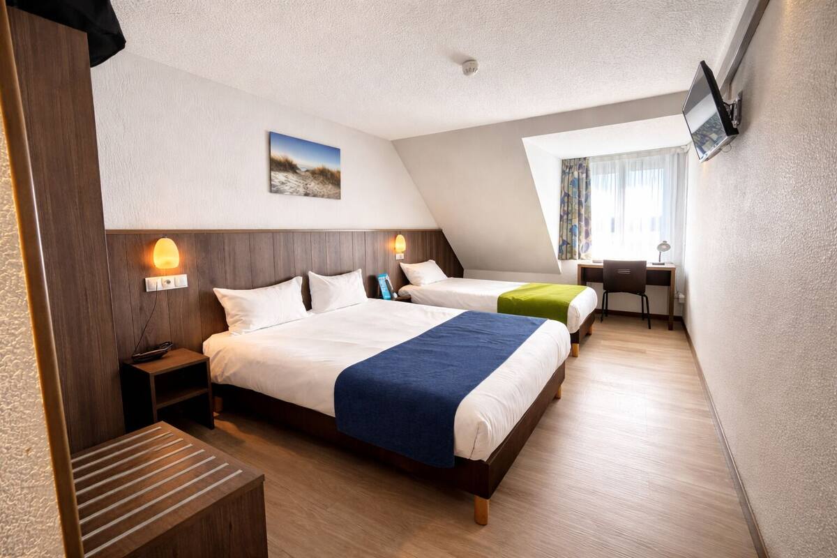 A hotel room with two beds, a desk, a chair, a TV, and a picture on the wall.