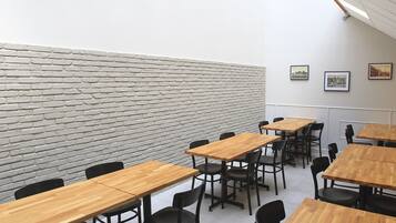 A conference room with wooden tables and black chairs, a white brick wall, and a skylight.