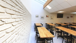 A classroom with white brick walls, wooden tables, and black chairs. - Brit Hotel Calais (Calais)