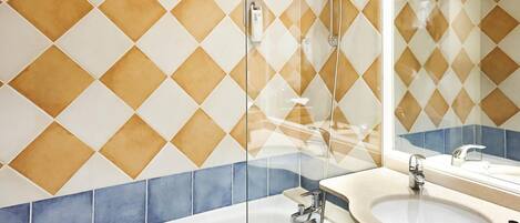 A bathroom with a tiled wall, a glass shower enclosure, a sink with a mirror, and a bathtub.